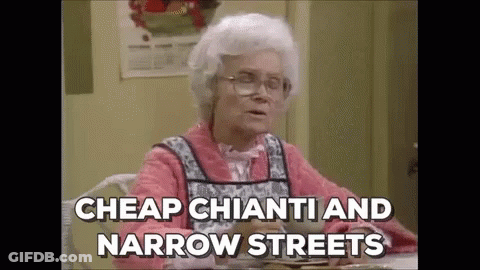 An Elderly Woman Is Sitting At A Table With A Plate Of Food And Saying `` Cheap Chianti And Narrow Streets `` . GIF