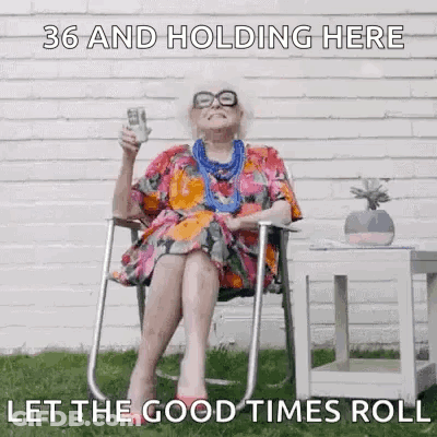 An Elderly Woman Is Sitting In A Chair Holding A Bottle Of Wine And A Dollar Bill . GIF