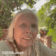 An Elderly Woman Is Smiling For The Camera While Standing In Front Of A Tree . GIF