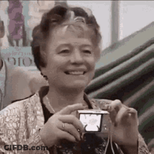 An Elderly Woman Is Smiling While Taking A Picture Of Herself With A Camera . GIF