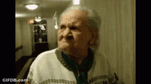 An Elderly Woman Is Standing In A Hallway And Making A Face . GIF
