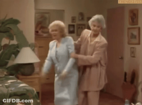 An Elderly Woman Is Standing In A Room Holding A Door Open . GIF
