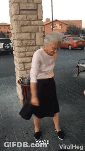 An Elderly Woman Is Standing In Front Of A Brick Wall Holding A Hat . GIF