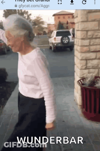 An Elderly Woman Is Walking Down A Sidewalk With The Word Wunderbar On The Bottom Of The Screen . GIF