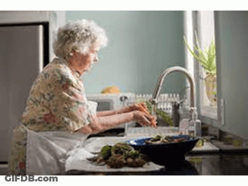 An Elderly Woman Is Washing Vegetables In A Sink In A Kitchen . GIF