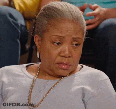 An Elderly Woman Wearing A Blue Shirt And A Gold Necklace Is Sitting In A Chair . GIF