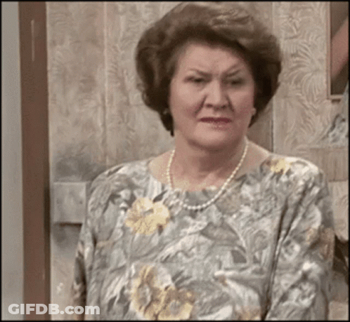 An Elderly Woman Wearing A Pearl Necklace And A Floral Shirt GIF