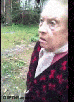 An Elderly Woman Wearing A Red And Black Sweater Is Standing In A Field GIF