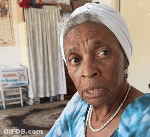 An Elderly Woman Wearing A White Turban And Pearls Looks At The Camera GIF