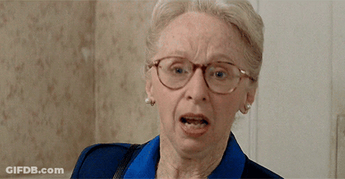 An Elderly Woman Wearing Glasses And A Blue Shirt Is Making A Funny Face GIF