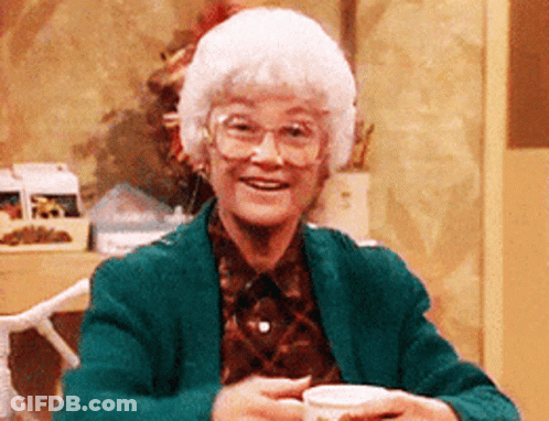 An Elderly Woman Wearing Glasses And A Green Jacket Holds A Cup Of Coffee GIF