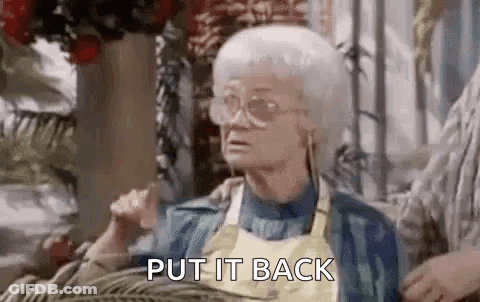 An Elderly Woman Wearing Glasses And A Yellow Apron Is Sitting On A Couch And Saying `` Put It Back '' . GIF