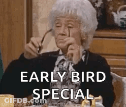 An Elderly Woman Wearing Glasses Is Sitting At A Table With A Cup Of Coffee And Says `` Early Bird Special '' . GIF