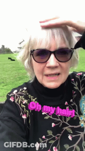 An Elderly Woman Wearing Sunglasses And A Black Shirt Says Oh My Hair GIF