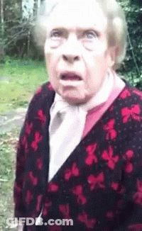 An Elderly Woman With A Surprised Look On Her Face Is Wearing A Red And Black Cardigan GIF