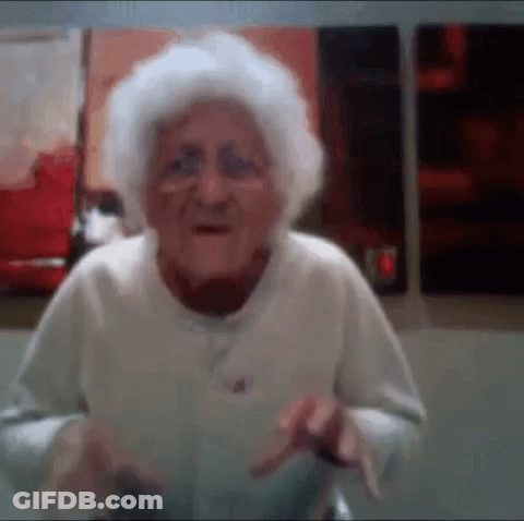 An Elderly Woman With Gray Hair Is Standing In Front Of A Wall . GIF