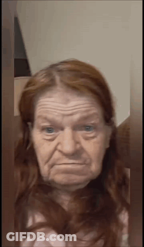 An Elderly Woman With Red Hair Is Making A Funny Face And Looking At The Camera . GIF