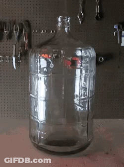 An Empty Glass Bottle Sits On A Table In Front Of Tools GIF
