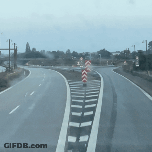An Empty Highway With A Red And White Chevron Sign In The Middle GIF