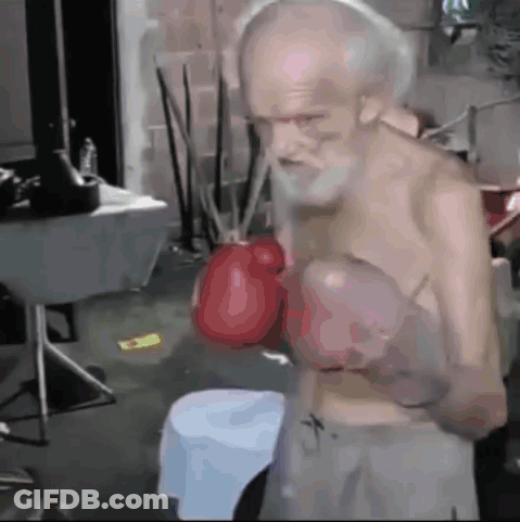 An Old Man With A Beard Is Wearing Boxing Gloves In A Room GIF