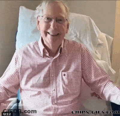 An Older Man In A Plaid Shirt Is Sitting In A Hospital Bed GIF