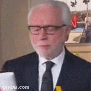 An Older Man In A Suit And Tie Is Looking At His Phone . GIF