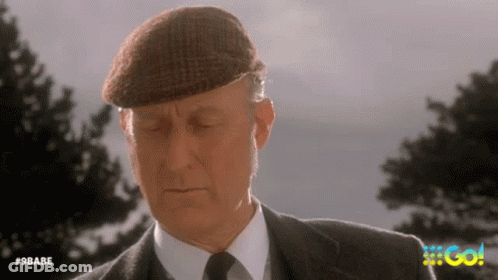An Older Man In A Suit And Tie Is Wearing A Hat And Looking Down . GIF