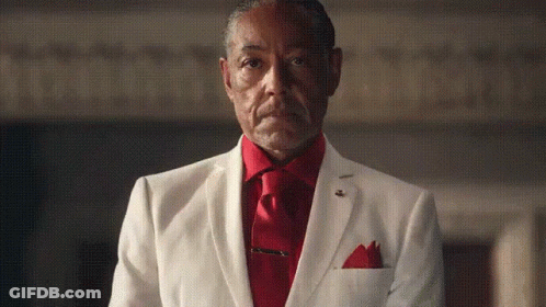 An Older Man In A White Suit And Red Tie Is Standing In A Dark Room . GIF