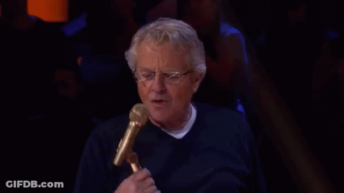 An Older Man Is Holding A Microphone And Talking Into It . GIF