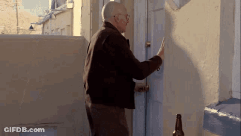 An Older Man Is Knocking On A Door With A Bottle Of Beer In Front Of Him . GIF