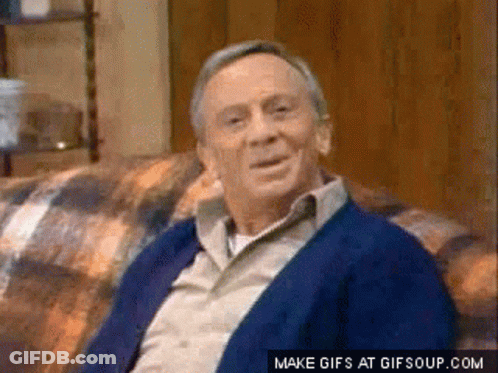 An Older Man Is Sitting On A Couch And Smiling . GIF