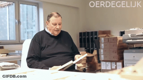 An Older Man Sits At A Desk Looking At A Book With The Word Oerdegelijk In The Corner GIF