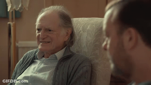 An Older Man Sitting In A Chair Talking To Another Man With The Word Gay On The Bottom GIF
