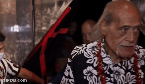An Older Man Wearing A Hawaiian Shirt Is Standing In Front Of A Car . GIF