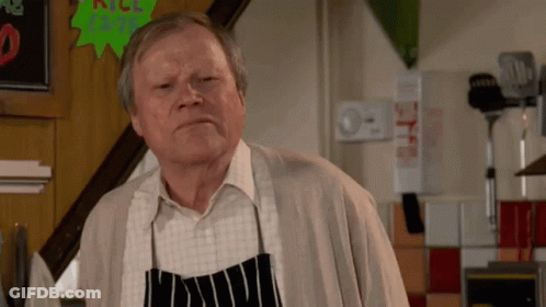 An Older Man Wearing An Apron Is Standing In Front Of A Sign That Says " All Beef " GIF