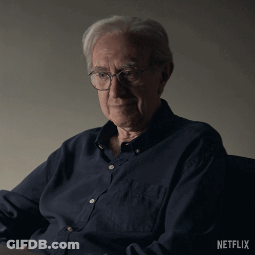 An Older Man Wearing Glasses And A Blue Shirt With The Netflix Logo On The Bottom GIF