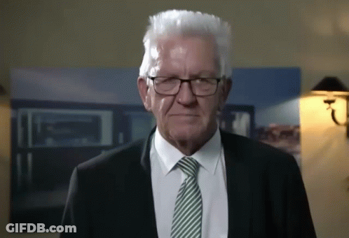 An Older Man Wearing Glasses And A Suit Is Looking At The Camera GIF