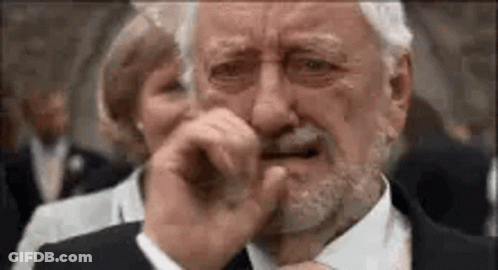 An Older Man With A Beard Is Crying And Covering His Mouth With His Hand . GIF