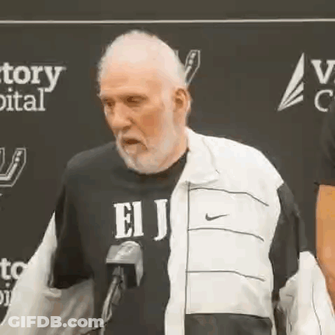 An Older Man With A Beard Is Standing In Front Of A Microphone . GIF