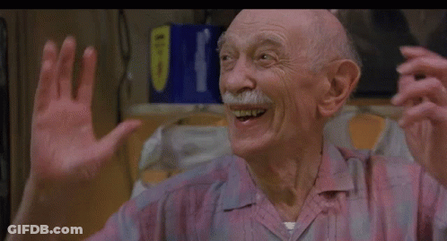 An Older Man With A Mustache Is Smiling And Waving His Hands In A Kitchen . GIF