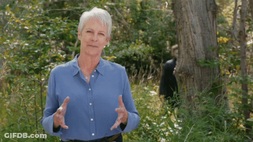An Older Woman In A Blue Shirt Is Standing In The Woods GIF