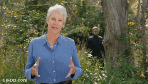 An Older Woman In A Blue Shirt Is Standing In The Woods Talking To Someone . GIF