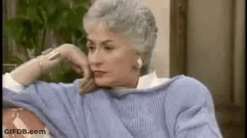 An Older Woman In A Blue Sweater Is Sitting On A Couch With Her Hand On Her Chin . GIF