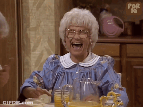 An Older Woman Is Laughing With A Pitcher Of Orange Juice In Front Of Her GIF