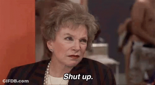 An Older Woman Is Saying `` Shut Up '' While Sitting In Front Of A Wall . GIF