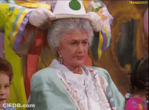 An Older Woman Is Wearing A Clown Costume And Holding A Hat On Her Head GIF