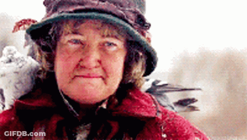 An Older Woman Wearing A Hat And A Red Coat GIF