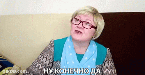 An Older Woman Wearing Glasses And A Blue Scarf Is Sitting On A Couch And Talking In Russian . GIF