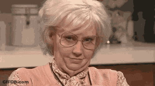 An Older Woman Wearing Glasses And A Pink Shirt Is Making A Funny Face . GIF