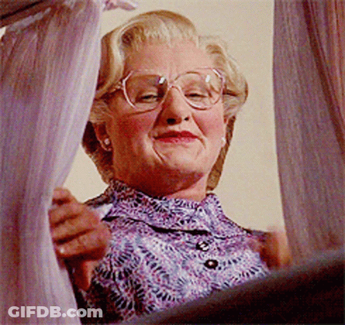 An Older Woman Wearing Glasses And A Purple Shirt Is Looking Out A Window GIF